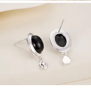 Pendientes de botón de plata con piedra negra ovalada y un pequeño colgante en forma de gota.