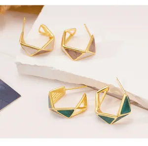 Primer plano detallado de pendientes de aro irregulares dorados con esmalte verde y blanco.