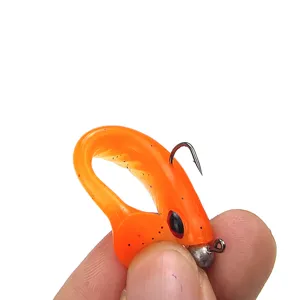 Primo piano di un'esca da pesca morbida arancione vivace con testa piombata e occhio realistico.