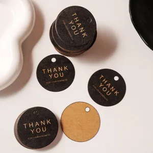 Detail shot of round black and kraft thank you paper tags with gold foil text for gift packaging.