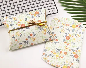 Vista dettagliata di scatole a cuscino in carta con motivo floreale e nastro dorato, confezione.