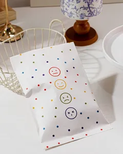 Dettaglio del sacchetto regalo in carta bianca con pois colorati e stampa di emoticon.