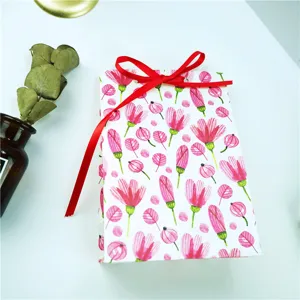Vista detallada de una bolsa de regalo de papel con diseño floral rosa y lazo rojo.