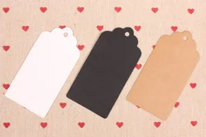 Close up detail of blank paper gift tags with wavy top design in white black and kraft colors.