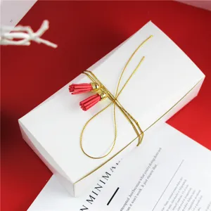 Boite d'emballage blanche en papier pour biscuits avec ficelle doree et glands rouges.
