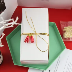 Vue détaillée d'un élégant coffret cadeau blanc avec ficelle dorée et glands rouges pour pâtisserie.