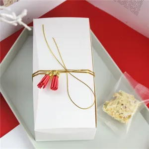 Détail de boîte d'emballage blanche pour nougat, boîte blanche élégante avec ficelle et pompons.