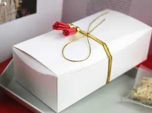Boite d'emballage blanche en papier avec ficelle doree et pompon rouge pour biscuits.