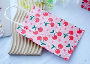 Piccola borsa regalo in carta rosa con ciliegie e pois bianchi, ideale per dolci e feste.