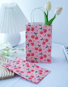 Dettaglio della borsa regalo di carta rosa con grazioso motivo a ciliegie e manici bianchi.