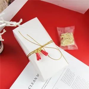 Boite cadeau en papier blanc avec cordon dore et pompons rouges pour biscuits et patisseries.