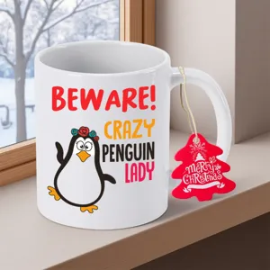 Nahaufnahme einer weißen Keramik Kaffeetasse mit süßem Pinguin Motiv und Weihnachtsetikett.