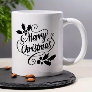 Nahaufnahme einer weißen Keramiktasse mit Frohe Weihnachten Aufdruck und weihnachtlichen Details.