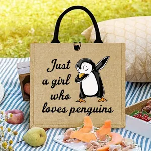 Charming penguin print detail on durable jute tote bag, perfect for outdoor picnic scenes.
