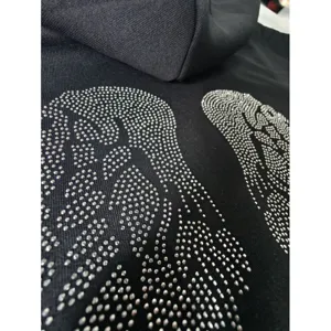 Close-up detail shot of black cotton hoodie featuring sparkling rhinestone angel wings.