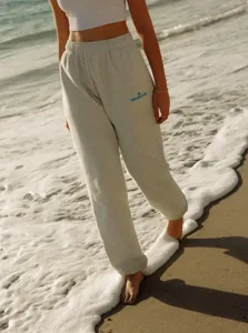 Detailed shot of casual heather grey joggers with blue embroidery, styled on beach background.