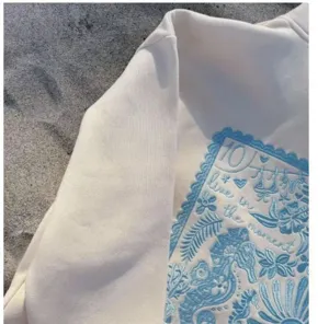 Detail view of a stylish white sweatshirt featuring delicate blue ocean embroidery and text.