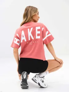 Maglietta oversize rosa a maniche corte con stampa di lettere bianche sul retro.