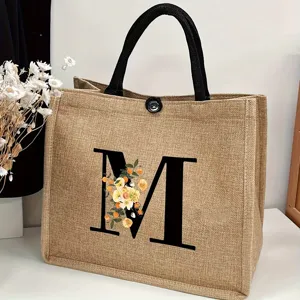 Detailed view of the jute tote bag featuring letter M and floral print with black handles.