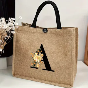 Detail shot of a large burlap tote bag featuring a floral letter A print and black handles.