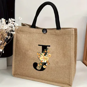 Close-up detail shot of a custom burlap jute tote bag with floral letter J print and handles.