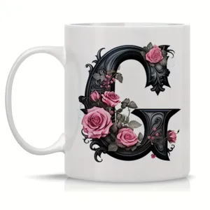 Close-up of white ceramic coffee mug featuring gothic letter G and pink rose floral design.