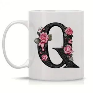 Detailed view of white ceramic coffee mug featuring ornate black letter Q with pink roses design.