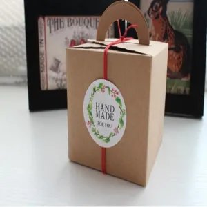 Vista detallada de la caja de regalo en papel kraft marrón con asa y cinta roja.