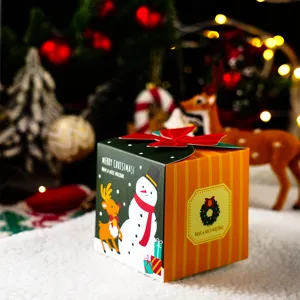 Primer plano de caja de regalo navideña con estampado de muñeco de nieve, lazo y luces de fondo.