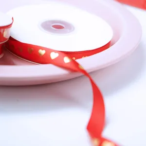 Gros plan détaillé d'un ruban cadeau rouge avec des motifs de cœurs dorés pour emballage festif.