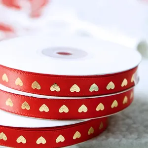 Détail en gros plan d'un ruban rouge avec des cœurs dorés, idéal pour les emballages cadeaux.