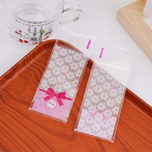 Transparente selbstklebende Keks Bonbonbeutel mit Spitzenmuster und rosa Schleife.