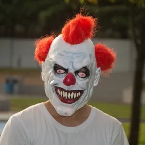 Scary clown mask detail showing white face, red hair puffs, and frightening sharp teeth.