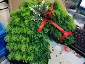 Handgemaakte kerst paardenhoofd krans detail, kunstmatige naaldtakken en rode strikversiering.