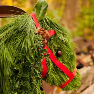 Handgemaakte kerst paardenhoofd krans detail met dennennaalden, dennenappels en rode lint.