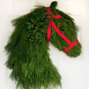 Handgemaakte kerstkrans in de vorm van een paardenhoofd met dennentakken en rood lint.