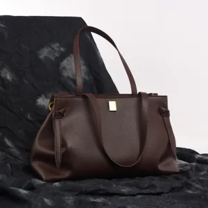 Detailed view of dark brown leather tote bag showing golden clasp and textured surface.