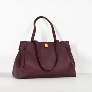 Burgundy leather tote bag detail showcasing pebble texture, dual top handles and metal clasp.