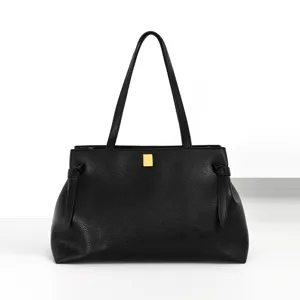 Detailed view of black leather tote bag featuring elegant side knots and a chic gold metal clasp.