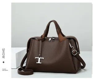 Detailansicht der braunen Ledertasche mit Narbenmuster, T-Metallanhänger und Henkeln.