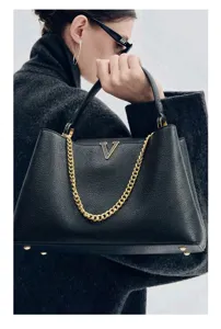 Black leather top handle handbag with gold chain detail and metal V hardware accent.