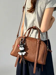 Detail view of the brown leather shoulder bag with a cute puppy keychain and stylish straps.