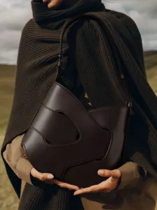 Close-up detail of dark brown cut-out leather shoulder bag, unique niche designer style.