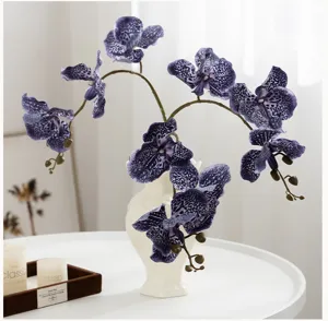 Vue détaillée de fleurs d'orchidées violettes tachetées artificielles dans un vase blanc.