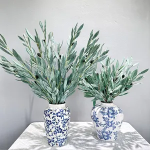 Kunstmatige olijftakken met zwarte vruchten in blauwwitte porseleinen vaas voor thuisdecoratie.