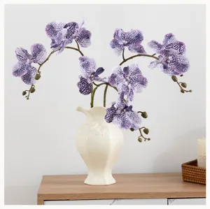 Arrangement de fleurs d'orchidée violettes artificielles dans un vase en céramique blanche