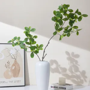 Artificial green leaves plant branch with white ceramic vase for home decor tabletop.