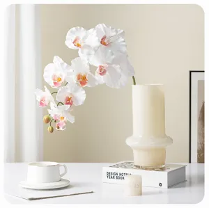 Detail view of artificial white orchid flowers in a modern cream vase with home decor props.