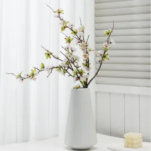Artificial peach blossom branches in white ceramic vase for home decor and photography.