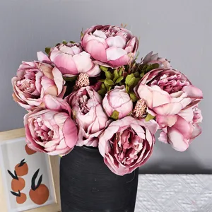 Gros plan d'un bouquet de pivoines artificielles dans un vase noir avec des feuilles et pétales.
